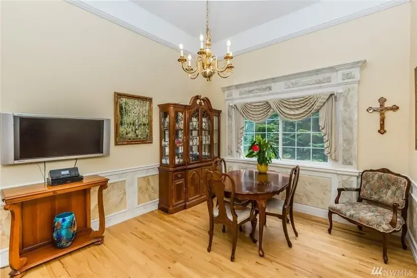 The dining room at A Rose Garden, with a chandelier over a wood table set with a single red rose, a china cabinet, and a bright garden window