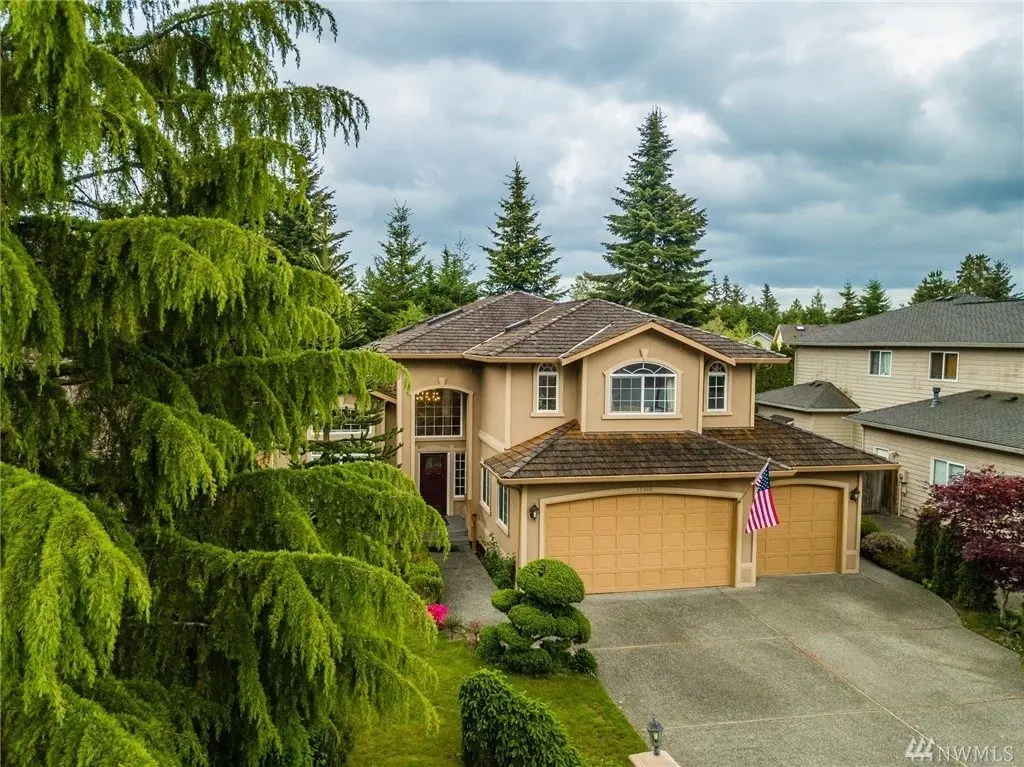 A Rose Garden Home 1 in Mill Creek, a two-story tan home with a three-car garage set among tall evergreens